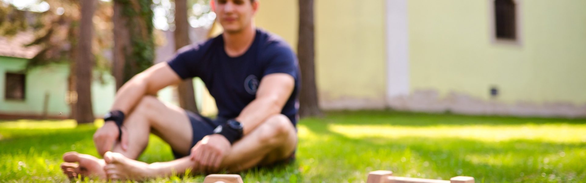 Christoph sitzt im Gras mit Parallettes vor ihm