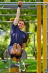Christoph hängt mit einem Arm an einer Klimmzugstange im L-Sit
